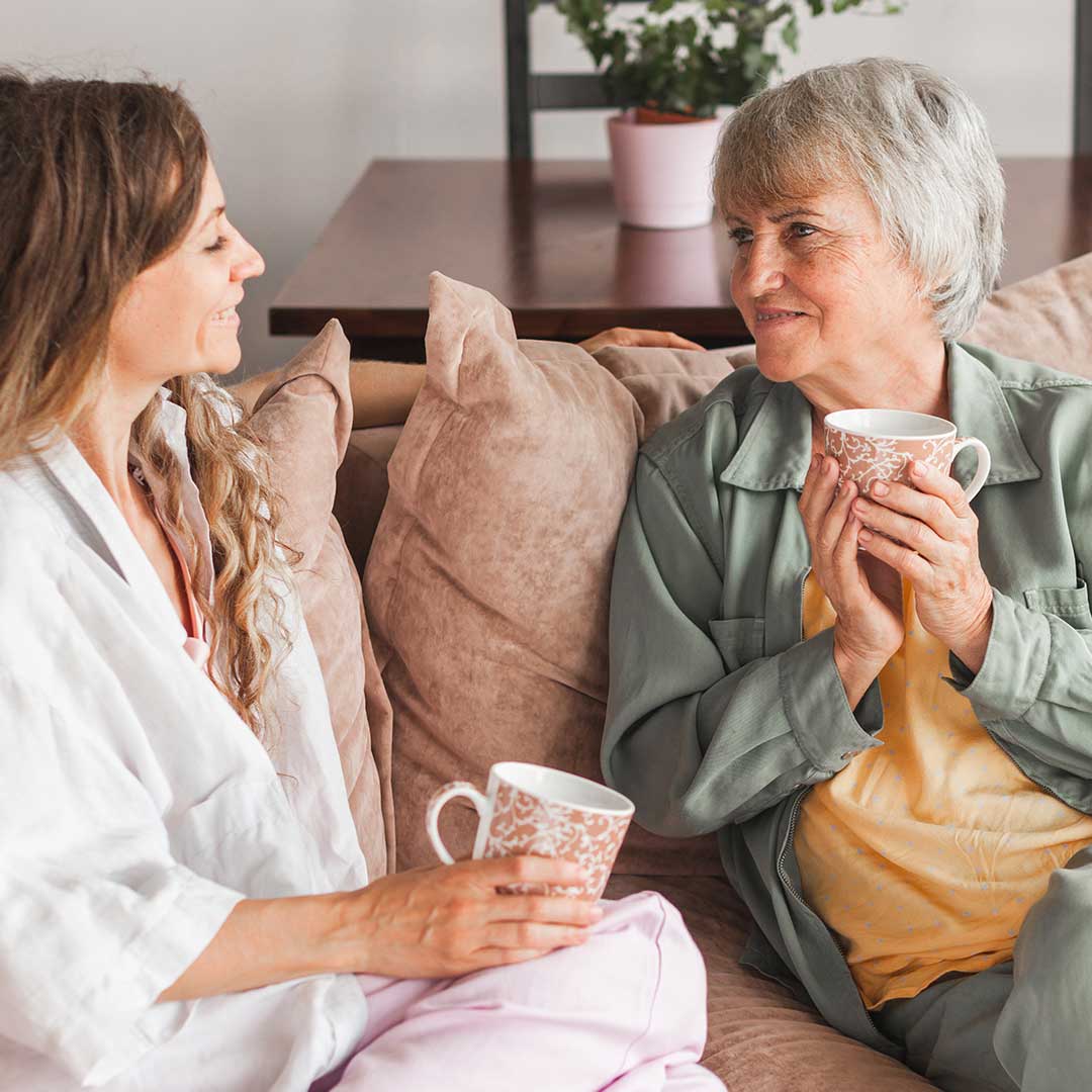 Hoitaja ja ikäihminen nauttivat kahvihetkestä yhdessä sohvalla